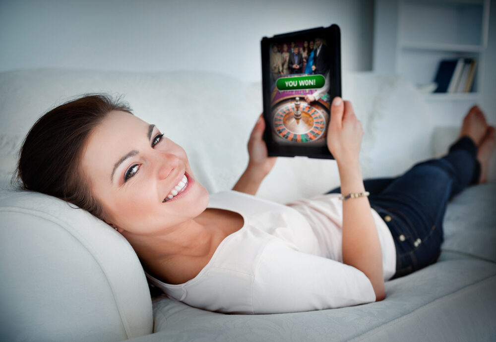 Een vrolijke en tevreden persoon die op zijn of haar smartphone kijkt, waarop een melding van een bank-app zichtbaar is met de tekst "Betaling ontvangen". Op de achtergrond is een wazige tablet met een casino-interface te zien, wat de link legt tussen de winst en de snelle ontvangst ervan.